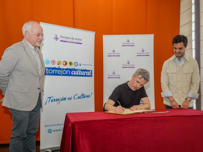 Momento de la firma de Juan Gómez-Jurado en el libro de Honor del Ayuntamiento de Torrejón ante la mirada del alcalde, Alejandro Navarro y el concejal de Cultura, José Antonio Moreno